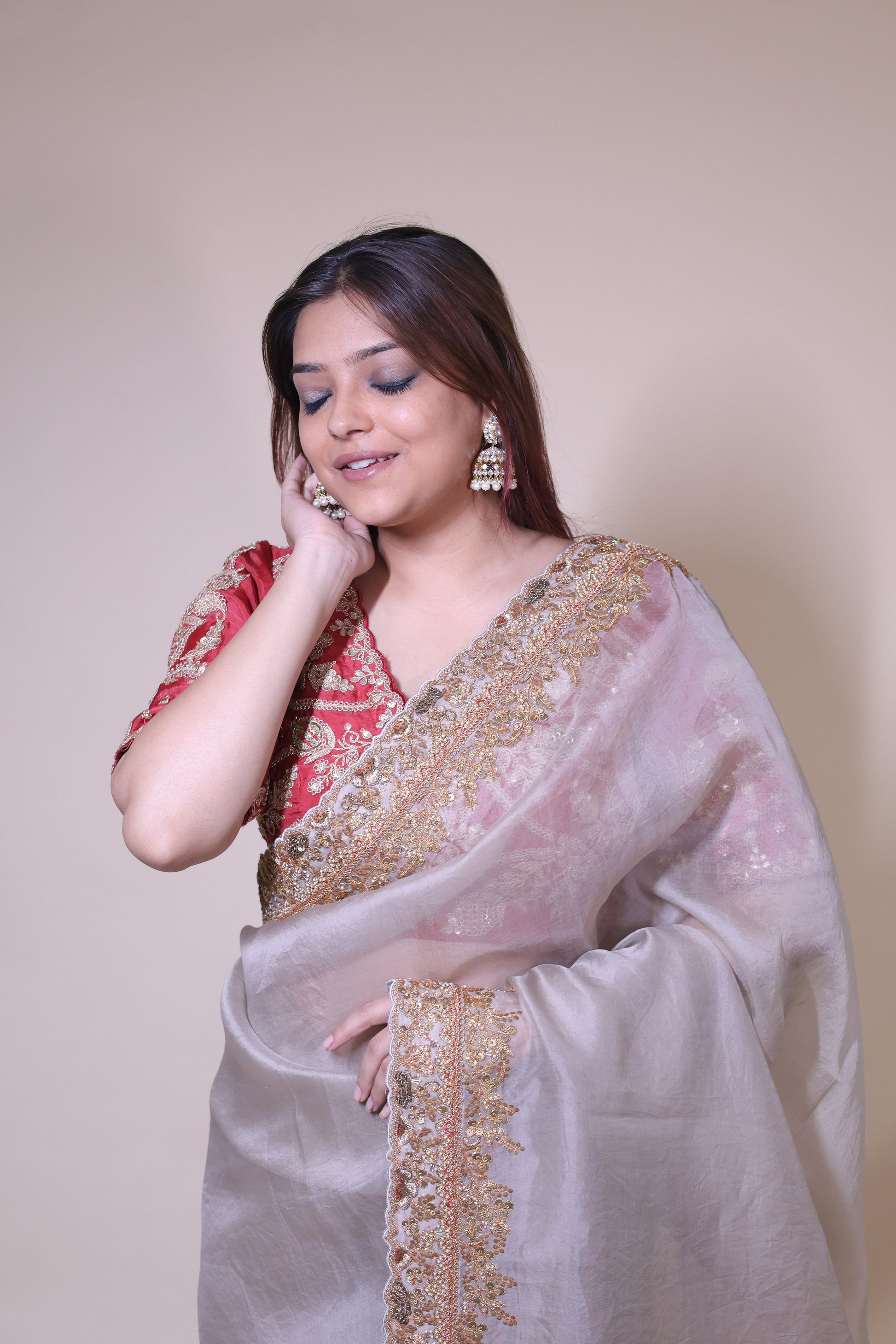 Woman wearing a traditional outfit with gold embroidery on a plain background Beige Organza Saree with Red Blouse