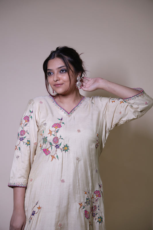 Woman wearing a white embroidered dress against a plain background Beige handpainted floral kurta with silk pallazzo suit with intricate dori & beads handwork