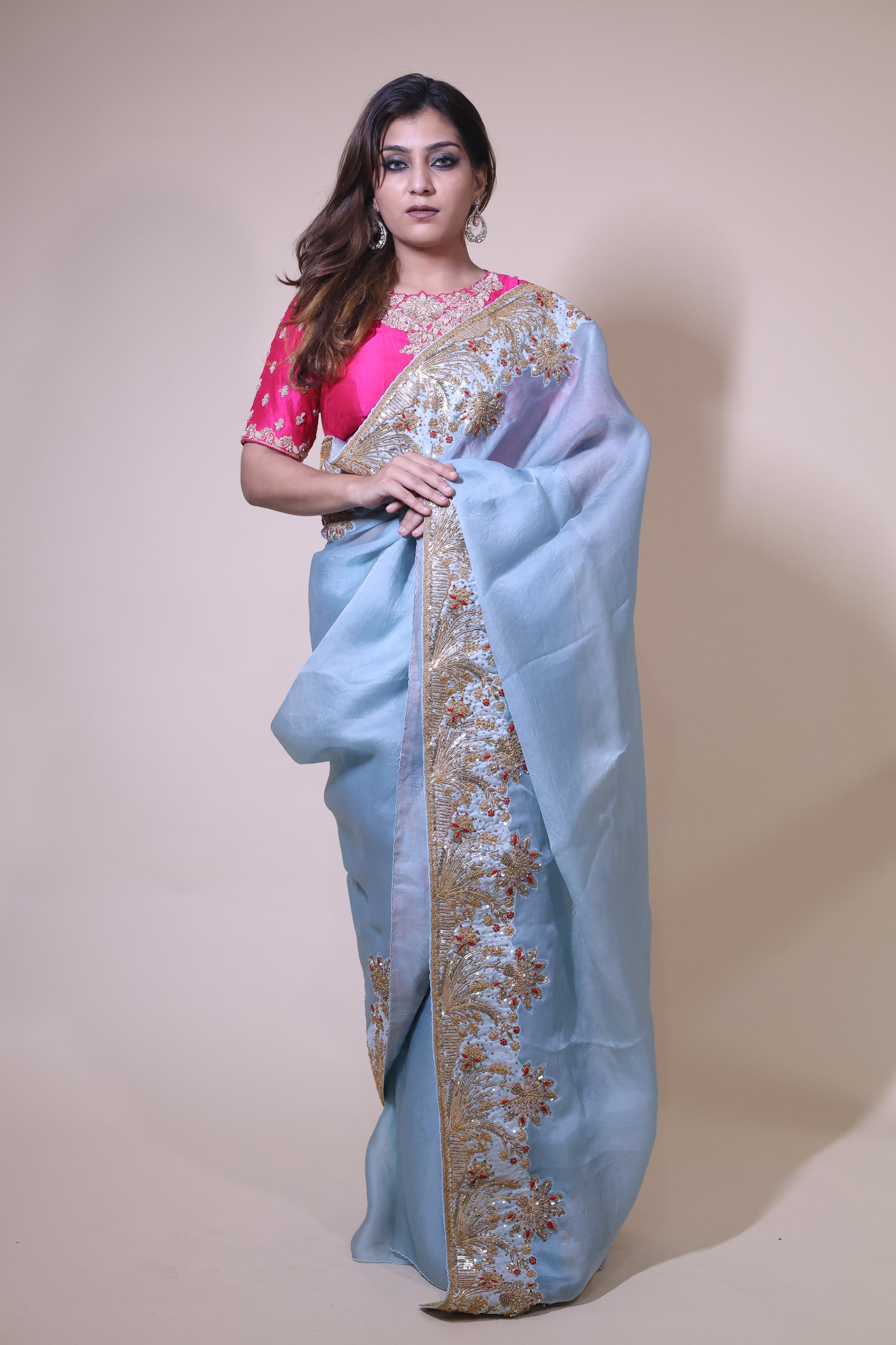 Woman wearing a light blue saree with gold embroidery on a beige background Blue Organza Satin Saree with pink blouse