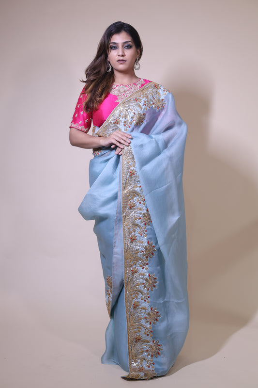 Woman wearing a light blue saree with gold embroidery on a beige background Blue Organza Satin Saree with pink blouse