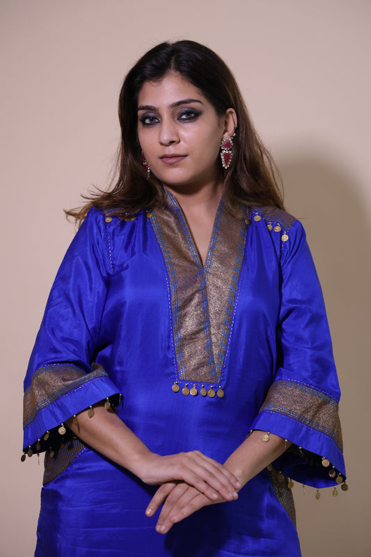 Woman wearing a blue traditional outfit with gold accents on a beige .Dark Blue Banarasi Silk Kurta Set with Mustard Pantsbackground