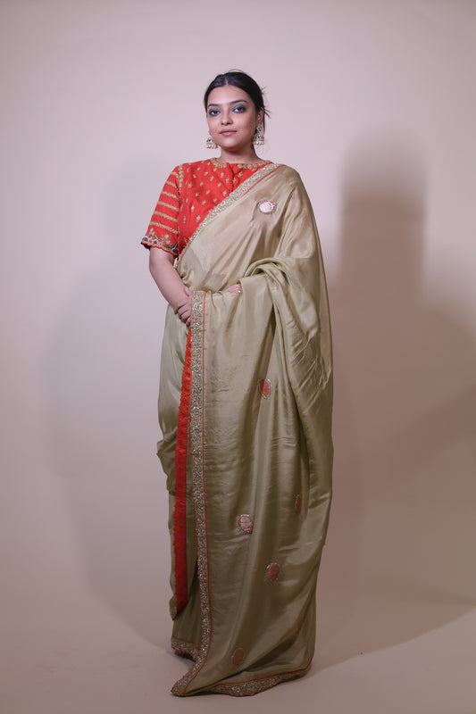 Woman wearing a traditional saree with a red blouse against a plain background Green Silk Zardozi Saree with Rust Blouse