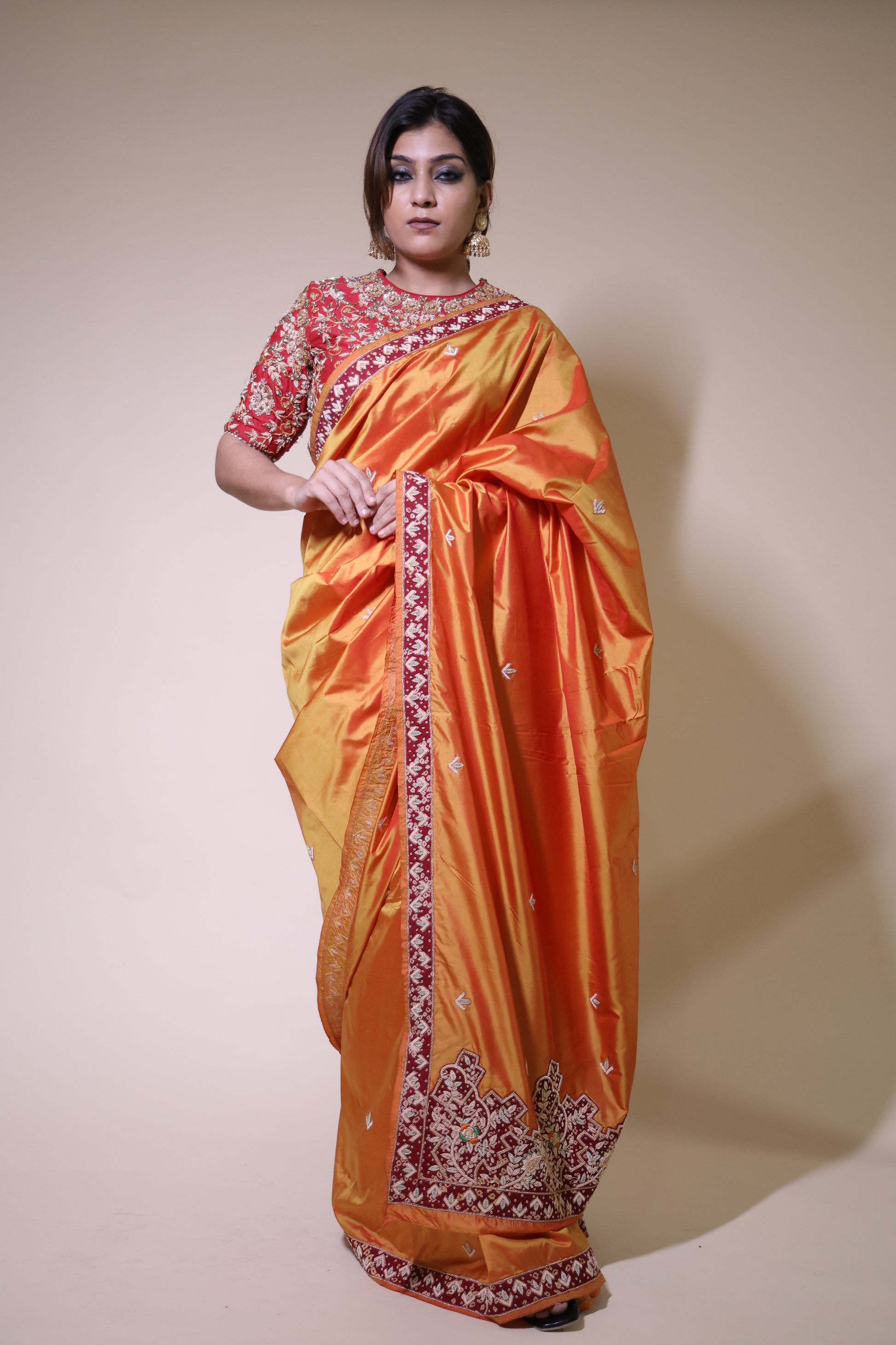 Woman wearing an orange saree with a red blouse against a beige background Mustard Gold Zardozi Saree with Red Blouse