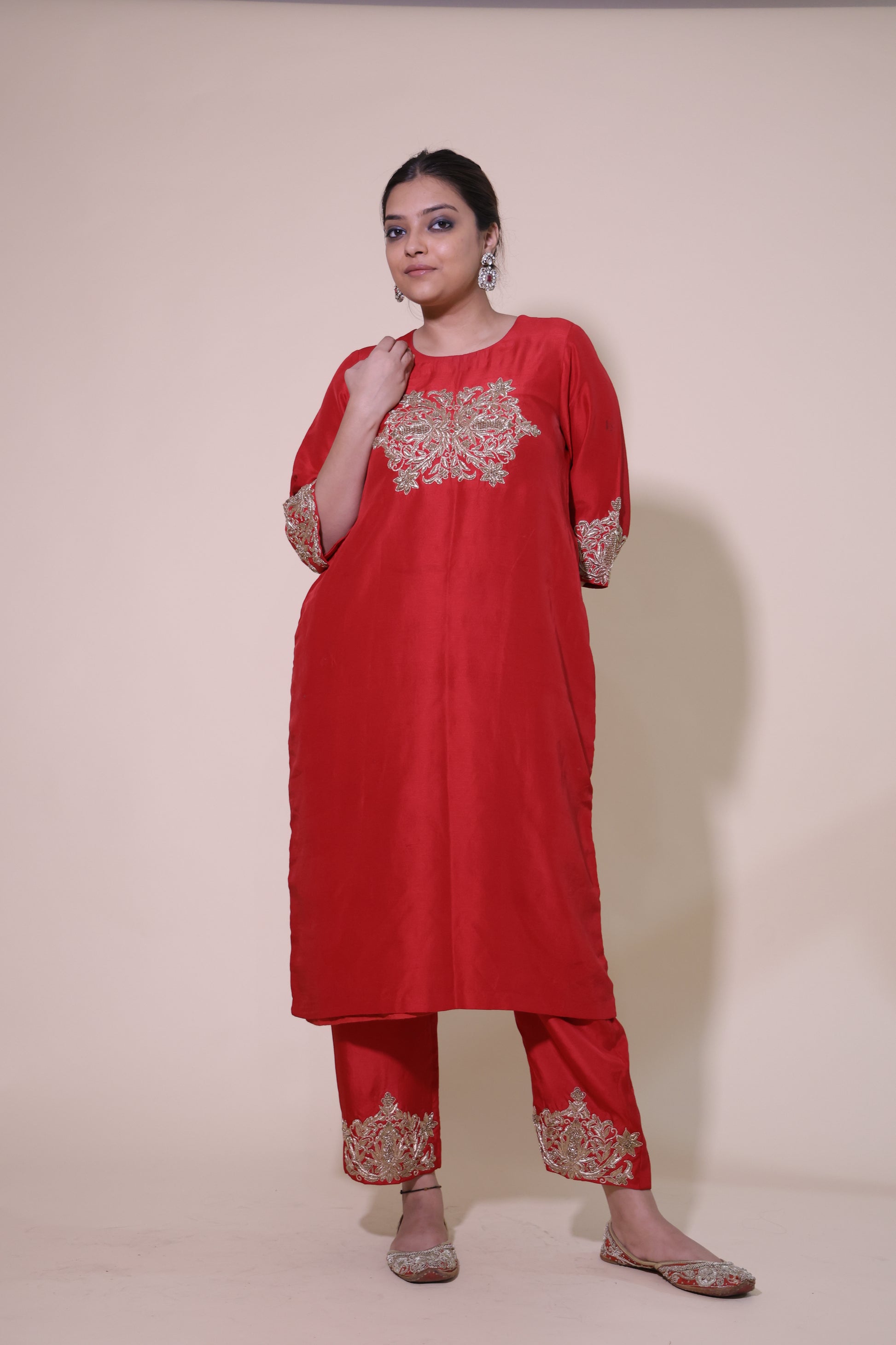 Woman wearing a red traditional outfit with gold embroidery on a beige background Red Pakistani Kurta with Zardosi Work and red pants